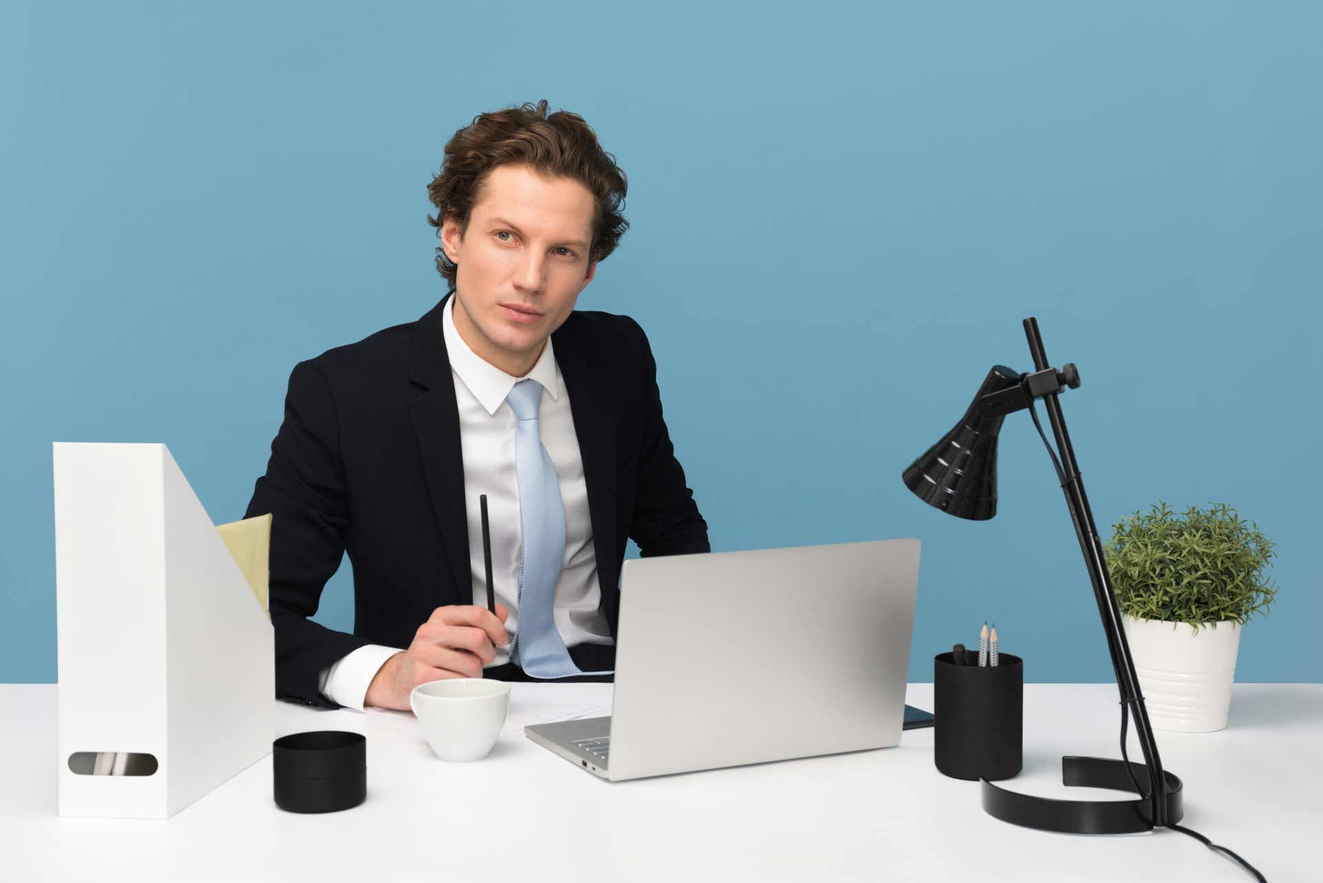 Mann sitzt auf einem Stuhl neben einem Laptop und einer Teetasse